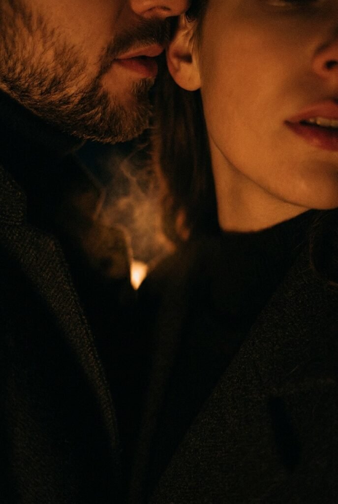 Two faces in warm amber darkness, lips near ear whispering — dirty talk intimacy, verbal arousal, sexual communication guide